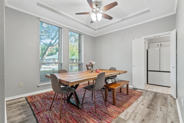 dining space with ceiling fan, a raised ceiling, crown molding, and light hardwood / wood-style flooring