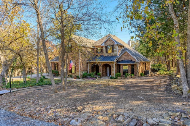 view of front of home featuring stone siding, covered porch, fence, and a chimney