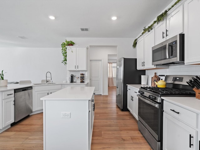 kitchen with sink, white cabinets, kitchen peninsula, stainless steel appliances, and light hardwood / wood-style flooring