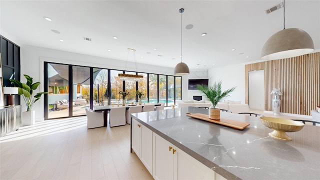 kitchen featuring white cabinetry, pendant lighting, light stone countertops, and light hardwood / wood-style flooring