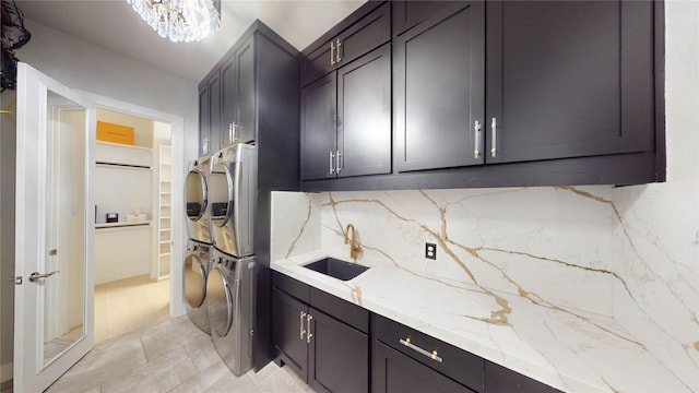 kitchen with sink, stacked washing maching and dryer, tasteful backsplash, light stone counters, and a notable chandelier