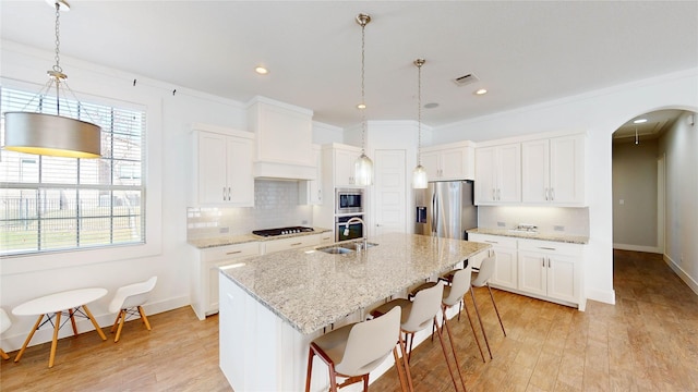 kitchen with white cabinetry, a center island with sink, stainless steel appliances, and light hardwood / wood-style floors