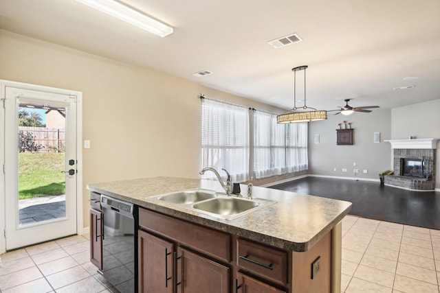 kitchen featuring pendant lighting, dishwasher, a kitchen island with sink, sink, and a fireplace