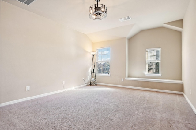 carpeted empty room featuring a notable chandelier and vaulted ceiling