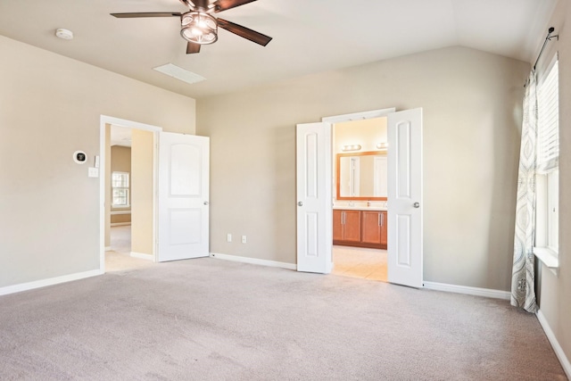 unfurnished bedroom featuring ceiling fan, sink, ensuite bathroom, light colored carpet, and vaulted ceiling