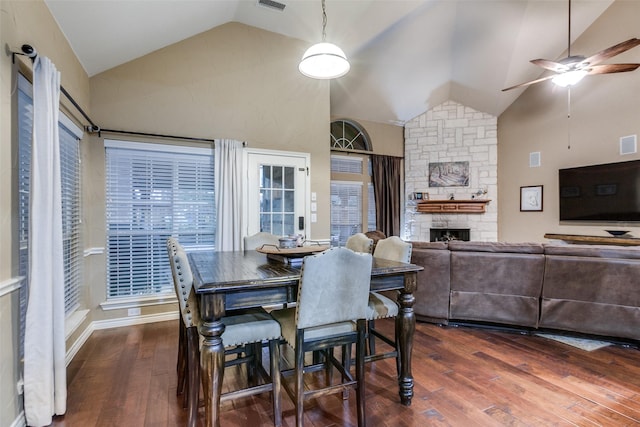 dining space featuring a stone fireplace, ceiling fan, dark hardwood / wood-style flooring, and high vaulted ceiling