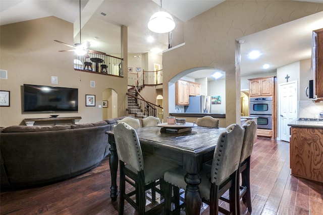 dining space with a high ceiling, ceiling fan, and dark wood-type flooring