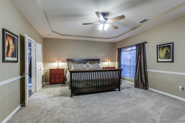 bedroom with ceiling fan, light colored carpet, and a tray ceiling