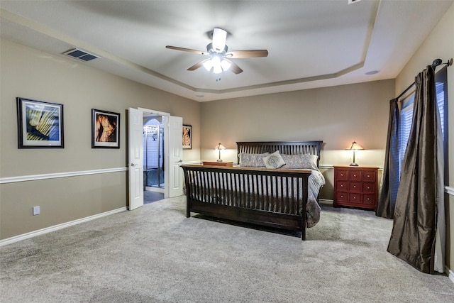 bedroom featuring a tray ceiling, ensuite bath, ceiling fan, and light colored carpet