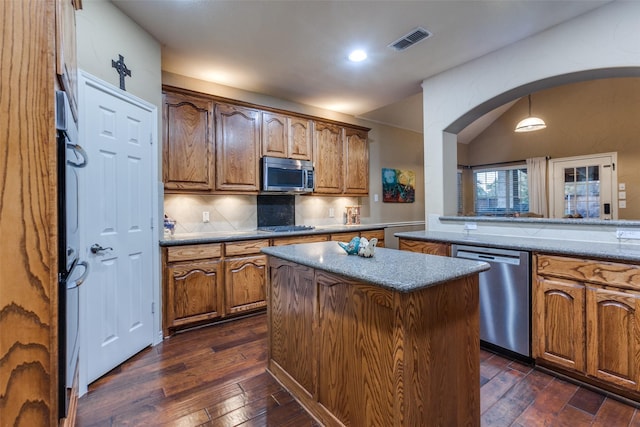 kitchen featuring dark hardwood / wood-style flooring, tasteful backsplash, stainless steel appliances, decorative light fixtures, and a center island