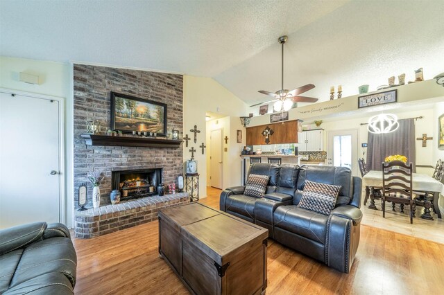 living room with ceiling fan, lofted ceiling, light hardwood / wood-style floors, and a brick fireplace