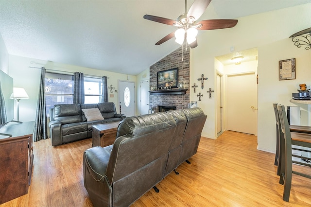 living room featuring ceiling fan, light hardwood / wood-style floors, vaulted ceiling, and a brick fireplace