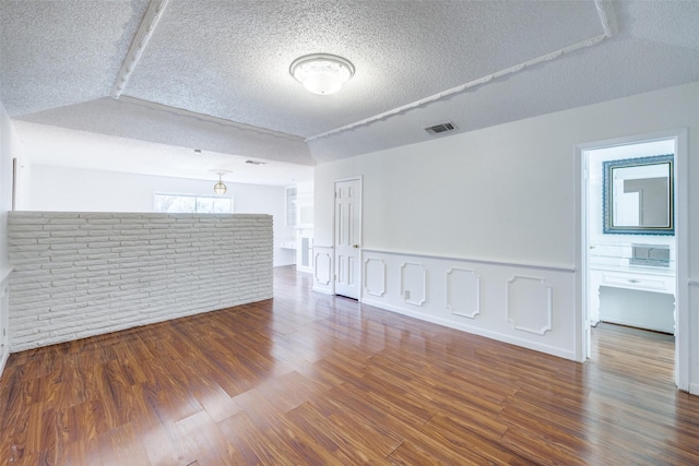 empty room with brick wall, a textured ceiling, and hardwood / wood-style flooring