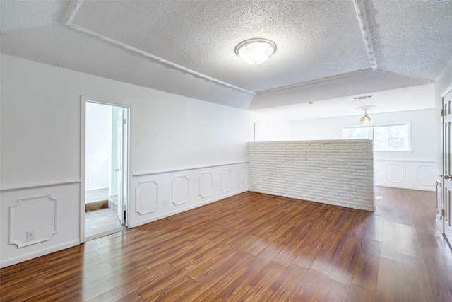 unfurnished room with vaulted ceiling, dark wood-type flooring, and a textured ceiling