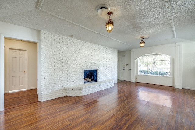 unfurnished living room featuring a textured ceiling, dark hardwood / wood-style flooring, a brick fireplace, and vaulted ceiling