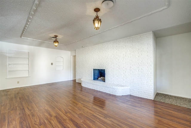 unfurnished living room featuring a textured ceiling, dark wood-type flooring, and a brick fireplace