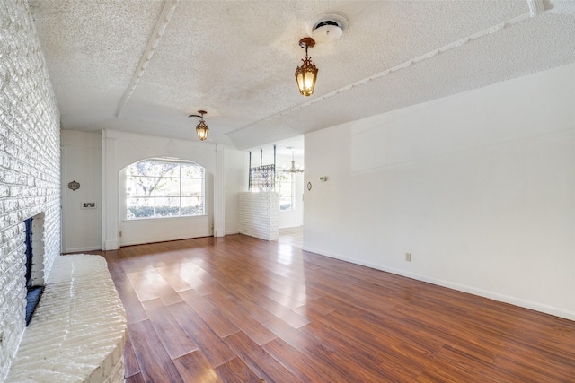 unfurnished living room with hardwood / wood-style flooring, an inviting chandelier, a textured ceiling, and a brick fireplace