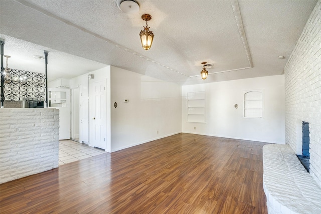 unfurnished living room with ceiling fan, a brick fireplace, brick wall, a textured ceiling, and light wood-type flooring