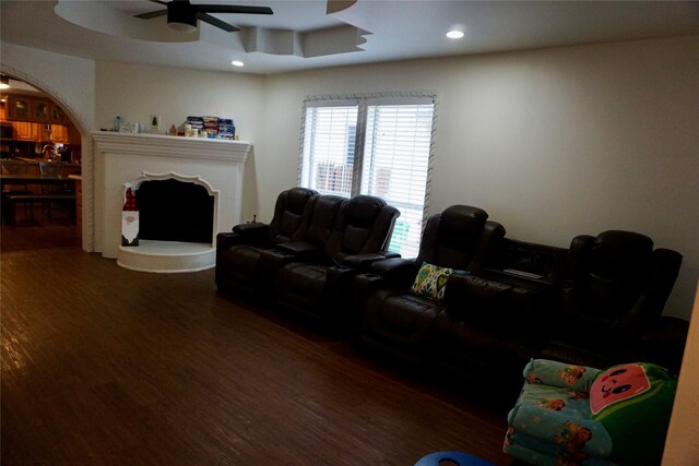 living room with a raised ceiling, ceiling fan, and dark wood-type flooring