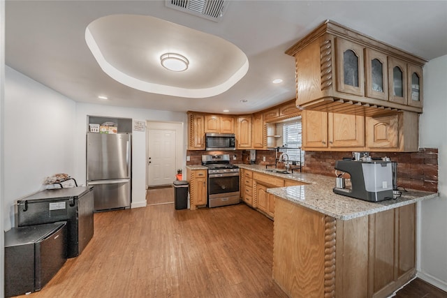 5613 Graham St, Sansom Park, TX 76114 - kitchen featuring appliances with stainless steel finishes, a sink, light wood-type flooring, light stone counters, and backsplash