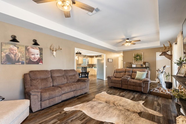 living room featuring ceiling fan, dark hardwood / wood-style flooring, and a tray ceiling