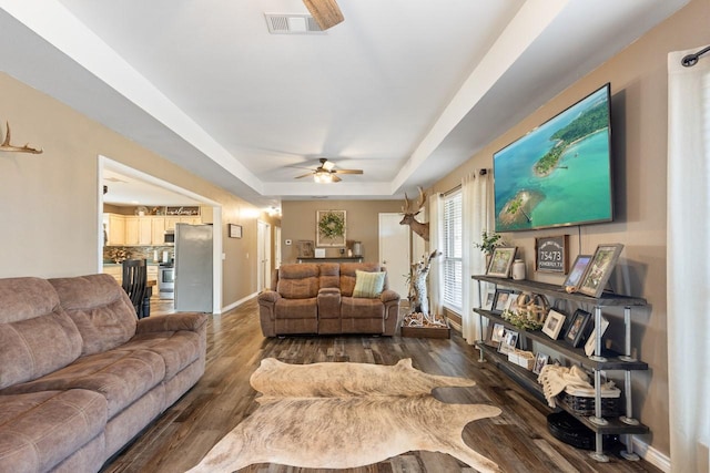 living room with a tray ceiling, ceiling fan, and dark hardwood / wood-style floors