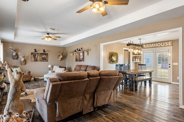 living room with a tray ceiling, dark wood-type flooring, and ceiling fan with notable chandelier