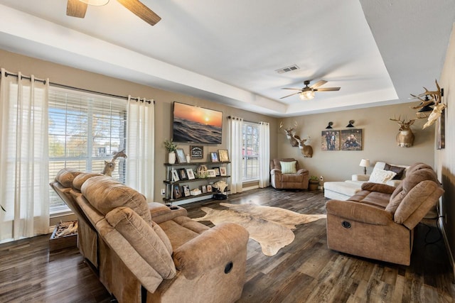 living room with a raised ceiling, ceiling fan, and dark hardwood / wood-style flooring