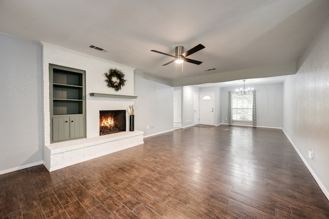 unfurnished living room featuring ceiling fan with notable chandelier, built in features, dark wood-type flooring, and a brick fireplace