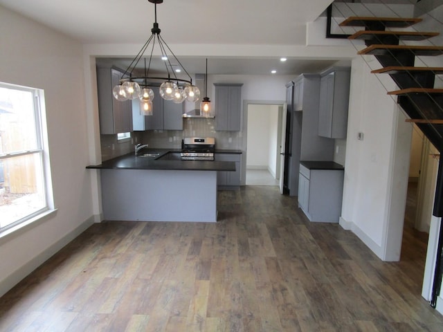 kitchen featuring pendant lighting, gray cabinetry, decorative backsplash, kitchen peninsula, and stainless steel range oven