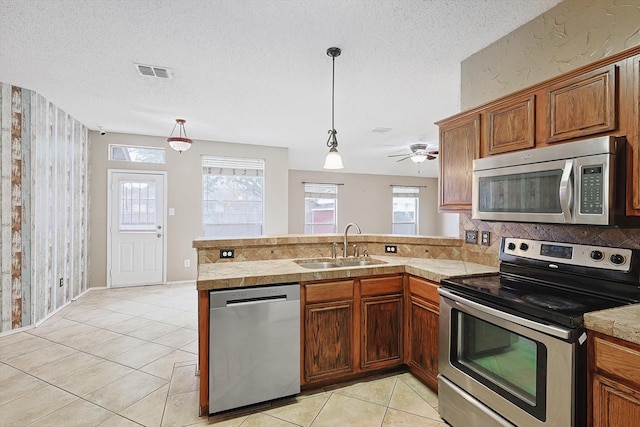 kitchen featuring a textured ceiling, appliances with stainless steel finishes, kitchen peninsula, and sink