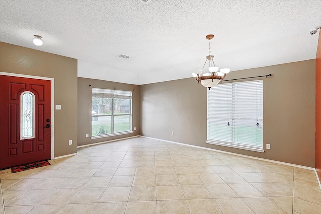 tiled entrance foyer featuring a textured ceiling and a chandelier