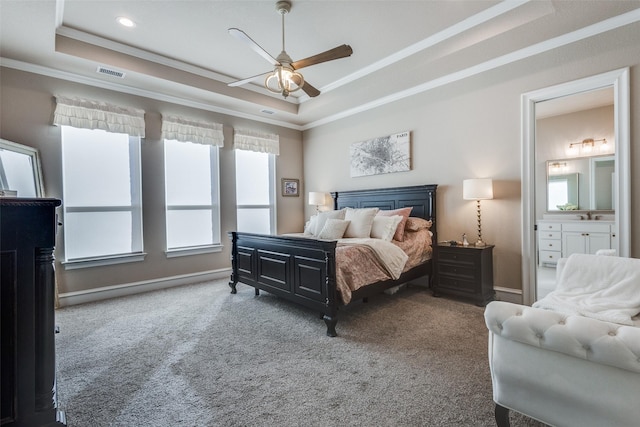 carpeted bedroom with ceiling fan, a raised ceiling, ornamental molding, and connected bathroom