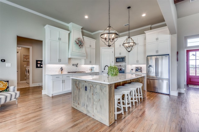 kitchen featuring a breakfast bar area, decorative light fixtures, appliances with stainless steel finishes, an island with sink, and white cabinets