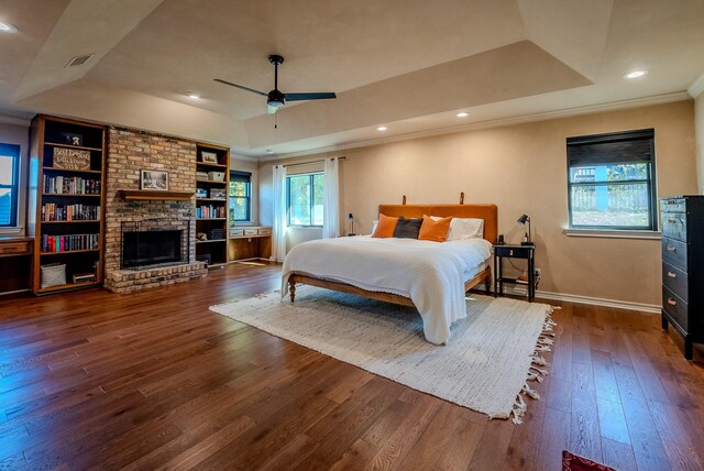 bedroom with ceiling fan, dark hardwood / wood-style flooring, a tray ceiling, a fireplace, and ornamental molding