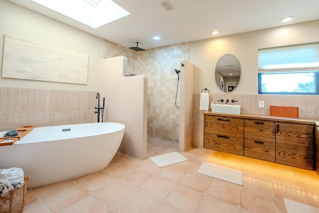 bathroom with vanity, plus walk in shower, a skylight, tile patterned flooring, and tile walls