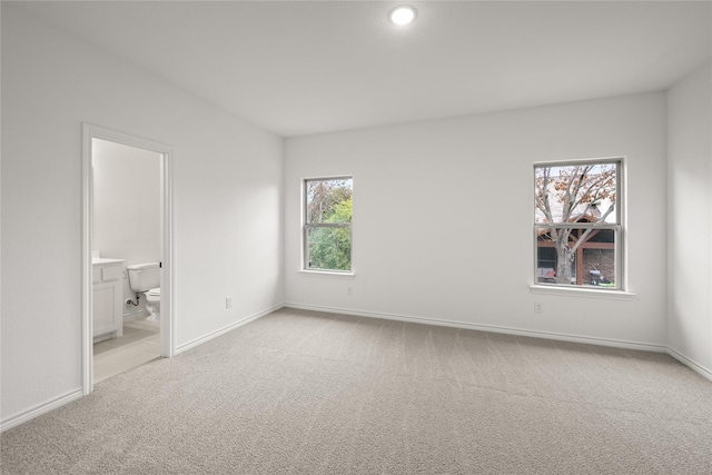 unfurnished bedroom featuring light colored carpet and ensuite bathroom