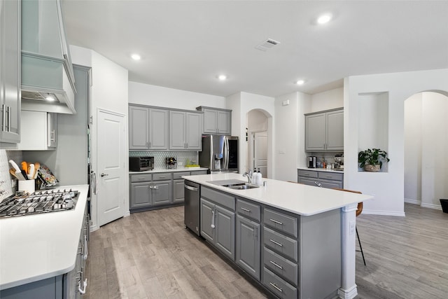 kitchen featuring gray cabinetry, a kitchen island with sink, appliances with stainless steel finishes, and tasteful backsplash