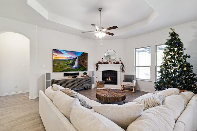 living room featuring light hardwood / wood-style floors, ceiling fan, and a tray ceiling