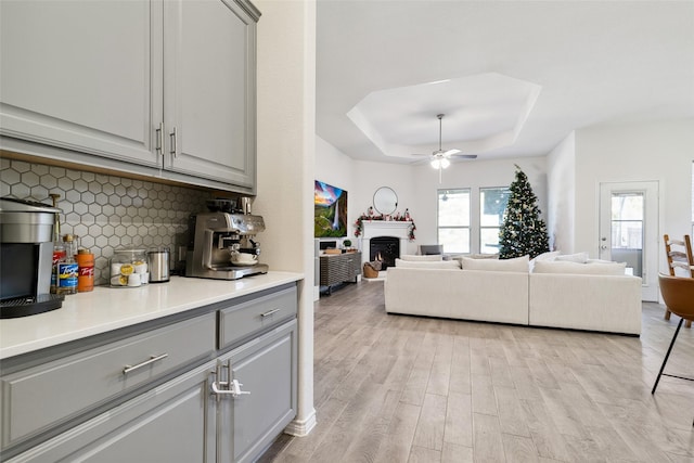 living room with ceiling fan, light wood-type flooring, and a tray ceiling