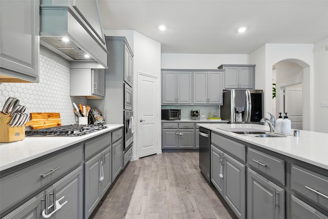 kitchen with appliances with stainless steel finishes, premium range hood, gray cabinetry, sink, and light hardwood / wood-style floors