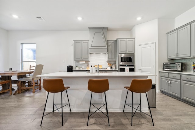 kitchen with a breakfast bar, stainless steel appliances, gray cabinetry, and an island with sink