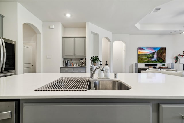 kitchen featuring gray cabinetry, an island with sink, and tasteful backsplash