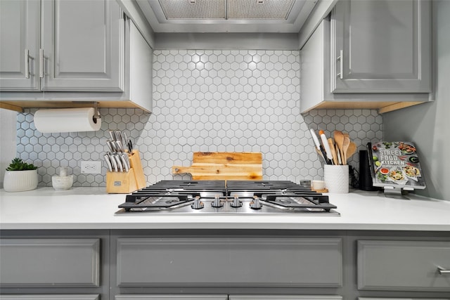 kitchen with gray cabinetry, exhaust hood, backsplash, and stainless steel gas cooktop