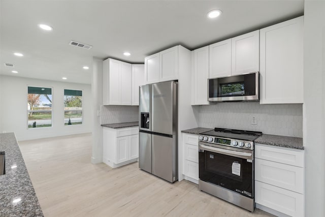 kitchen featuring appliances with stainless steel finishes, tasteful backsplash, dark stone countertops, white cabinets, and light hardwood / wood-style floors