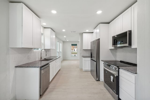 kitchen with white cabinetry, sink, stainless steel appliances, light hardwood / wood-style flooring, and dark stone counters