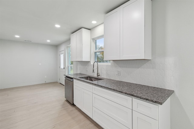 kitchen featuring stainless steel dishwasher, sink, dark stone counters, and light hardwood / wood-style flooring