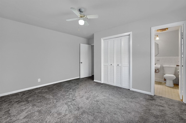 unfurnished bedroom with ensuite bathroom, dark carpet, tile walls, and ceiling fan