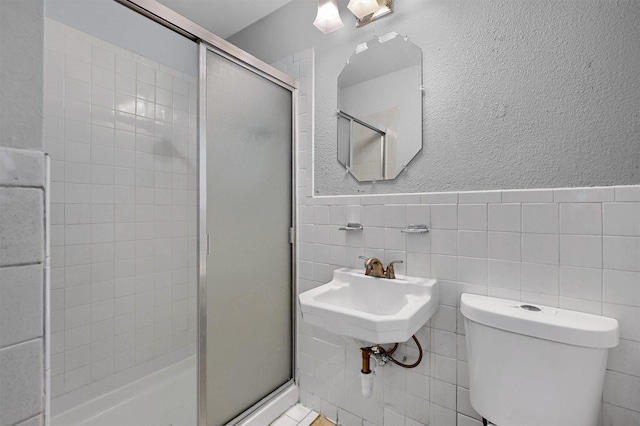 bathroom with toilet, tile walls, a shower with shower door, and sink