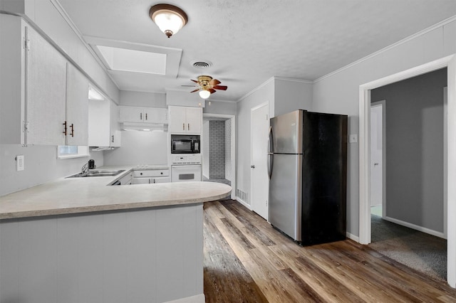 kitchen with stainless steel refrigerator, black microwave, oven, white cabinets, and light wood-type flooring